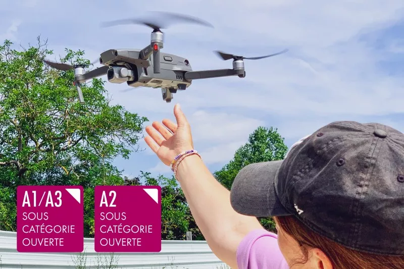 Drone à l'atterrissage dans la main d'une télépilote drone en extérieur avec les logos des scénarios des sous-catégories A1/A3 et A2